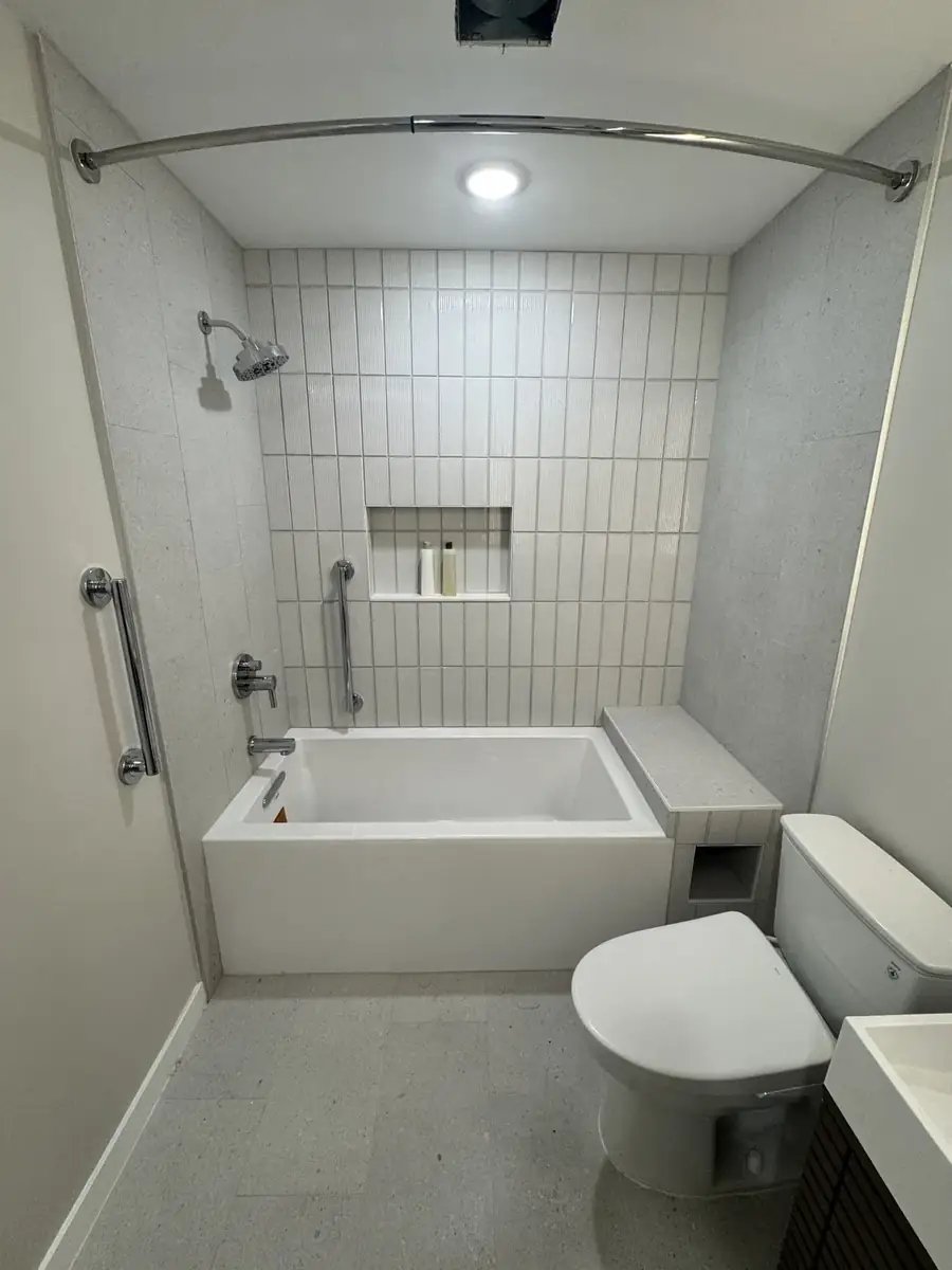 Completed bathroom renovation with tiled tub-shower surround, recessed niche, grab bars and built-in bench