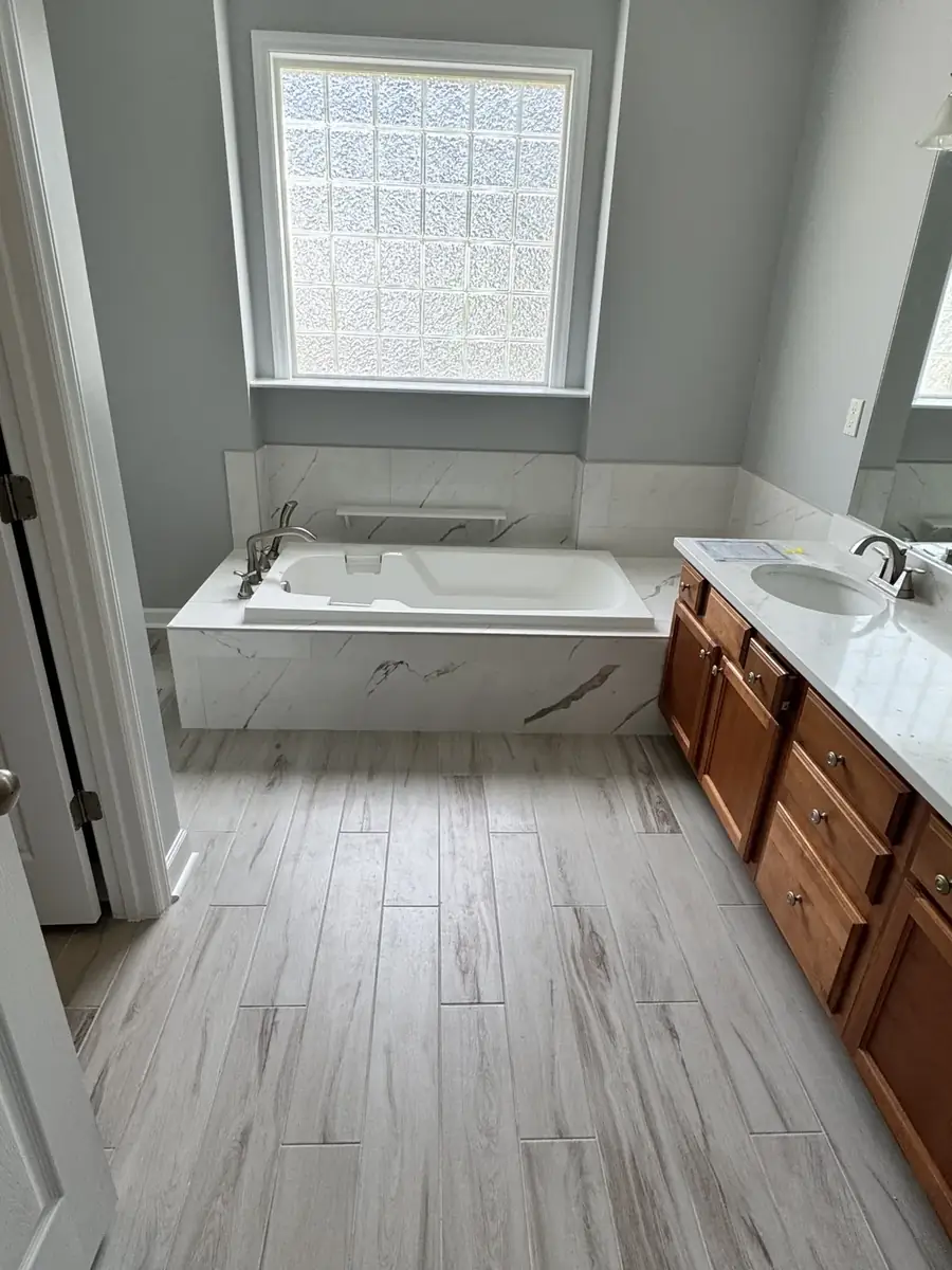 Finished bathroom renovation with tiled soaking tub surround and wood-look floor