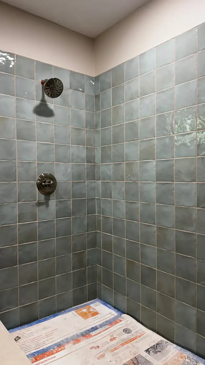 Blue-gray square tile custom shower walls with installed shower head and valve during finish work