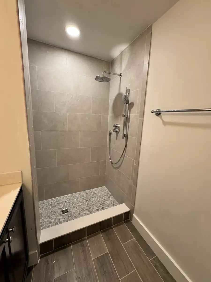 Gray tile walk-in shower with rain head, handheld fixture and pebble mosaic floor