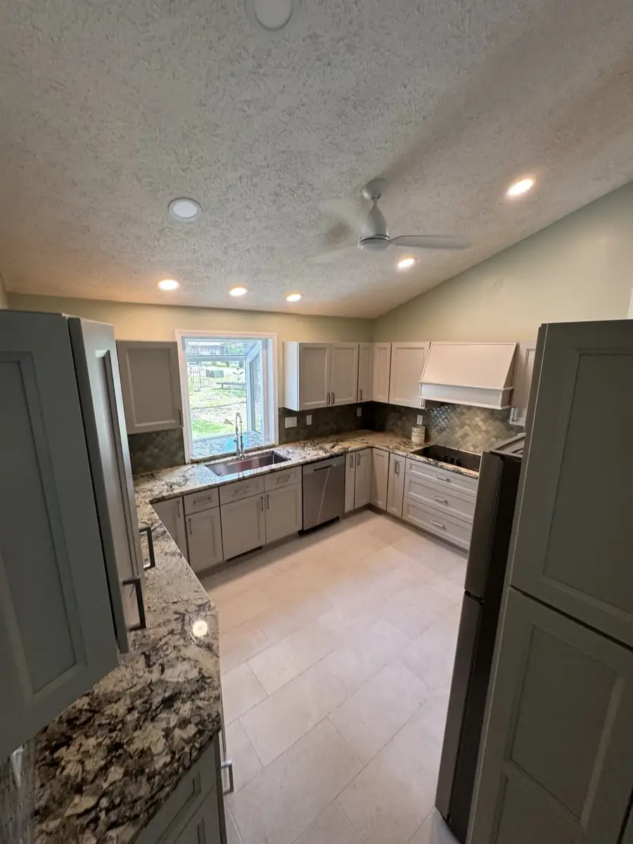 Wide finished kitchen with light cabinets, tile floor, granite counters and new lighting